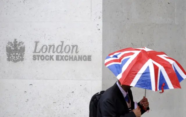 Man stands under umbrella outside of the London Stock Exchange