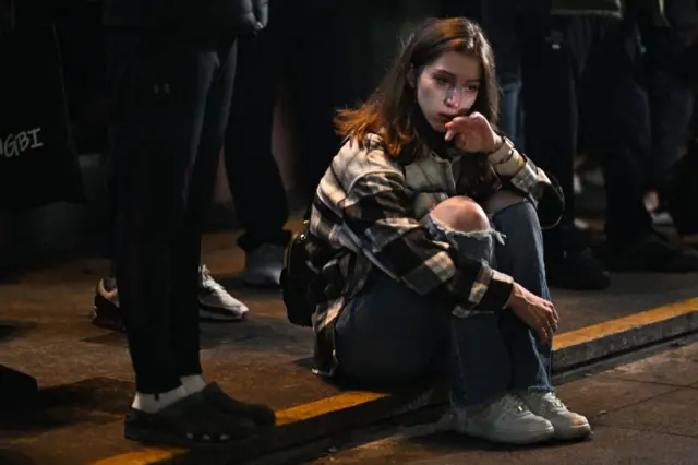 Woman sitting on pavement near the scene of Saturday night's crush