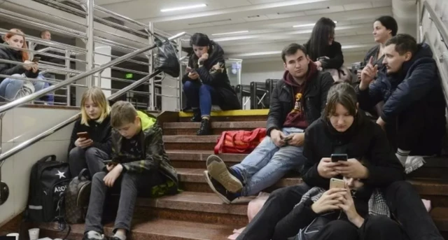 People check their phones as they shelter inside a metro station after a shelling in Kyiv