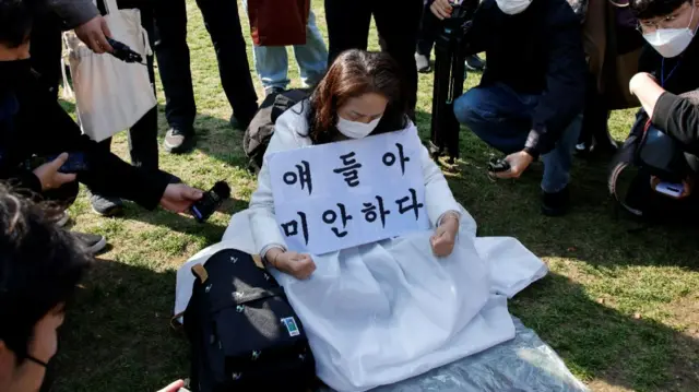 A woman reacts while holding a sign that reads "I am sorry" in front of a group memorial altar at Seoul City Hall Plaza in Seoul, South Korea, October 31, 2022. REUTERS/Heo Ran