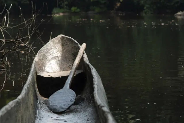 A wooden canoe parked on the edge of a tropical river in the tropical rainforest in Liberia, West Africa (stock photo)