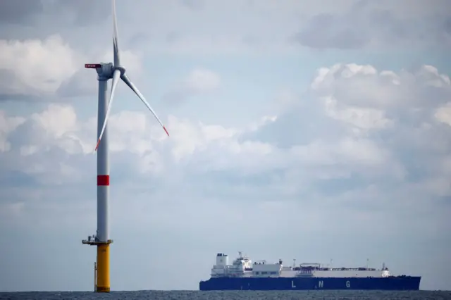 The liquefied natural gas (LNG) carrier Flex Rainbow sails near a wind turbine at the Saint-Nazaire offshore wind farm, off the coast of the Guerande peninsula in western France