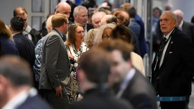 Attendees of the Conservative Party conference hold a conversation while standing in a queue