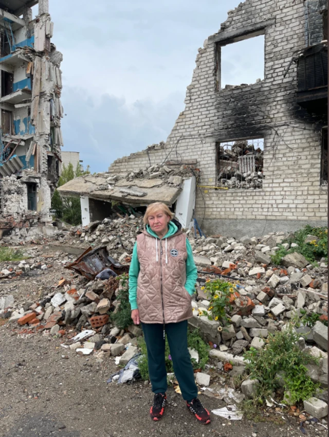 A woman stands in front of a ruined building in Ukraine