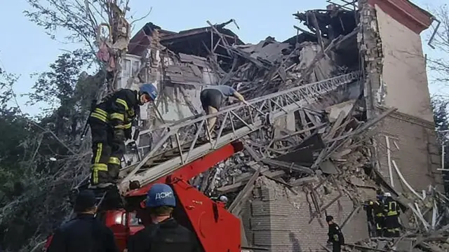 A person walks down an emergency services ladder from the rubble of a heavily damaged residential building in Zaporizhzhia