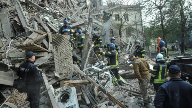 A number of emergency workers climb through rubble in Zaporizhzhia