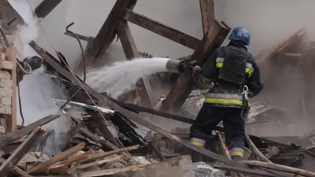 Firefighter sprays rubble with water from a hose