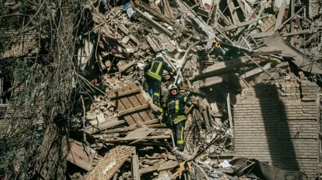 Ukrainian firefighters stand on the rubbles of a building looking for survivors after a strike in Zaporizhzhia on October 6, 2022