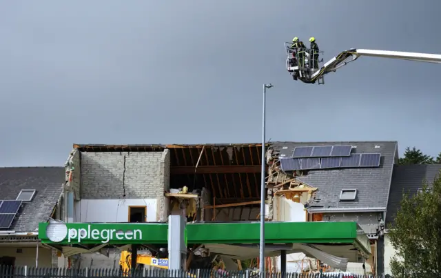 Firefighters on a mechanical platform assess the damage caused to the service station and a nearby apartment block