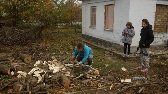 A boy saws wood for heating a damaged house in Kherson