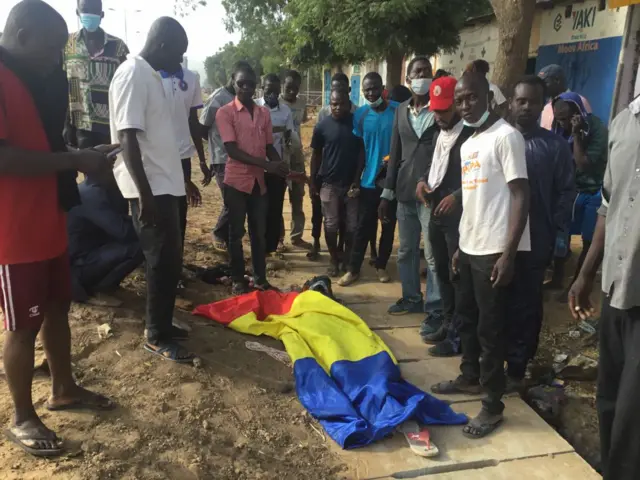 People in N'djamena stand next to the covered body of protester.