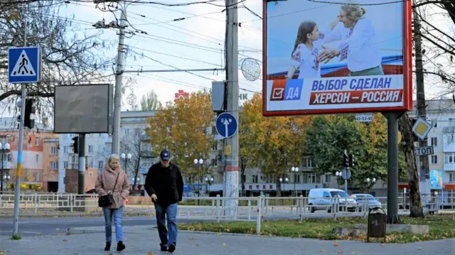 People walk along a street next to the banner reading "The choice is made. Kherson is Russia"