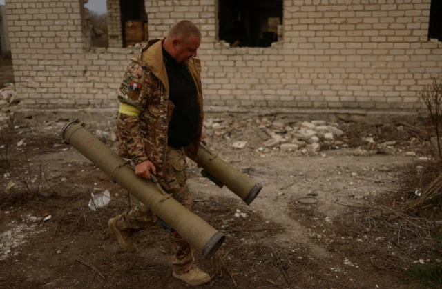 A Ukrainian serviceman carries captured anti-tank grenade launchers at a former position of Russian soldiers in the village of Blahodatne