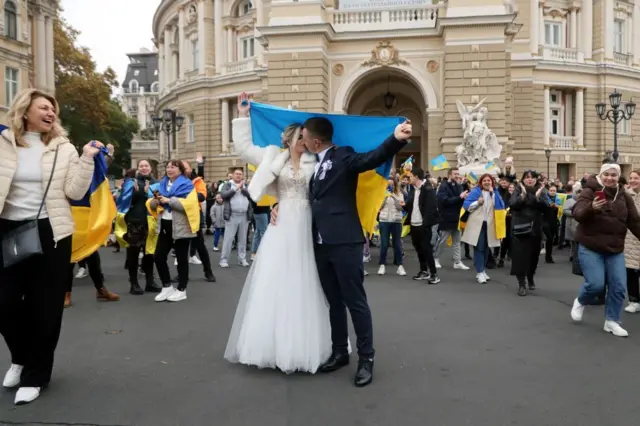 Newlyweds in Odesa, holding a Ukrainian flag, kiss as they celebrate the liberation of their home town of Kherson