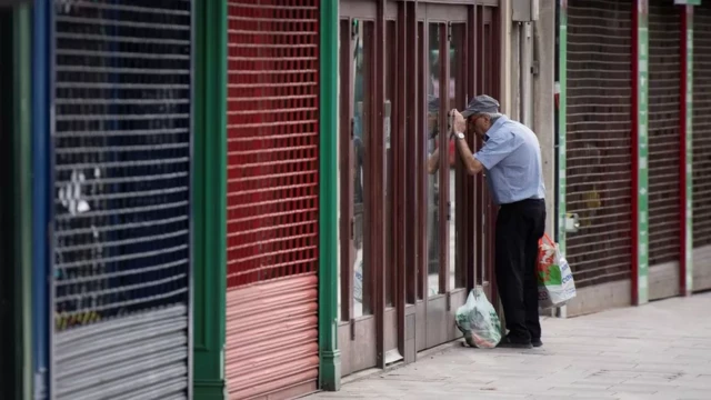 Man looking through the shutters on a closed down shop