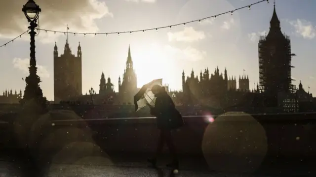 A pedestrian walks in the rain along Southbank past a view of the Houses of Parliament on October 31, 2021 in London, England