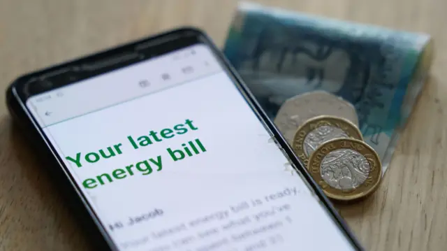 File photo of a phone showing an energy bill alongside some pound notes and coins