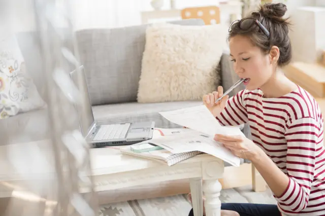 A stock image of a woman consulting her bills while sitting at a laptop