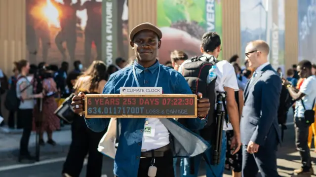 Nyombi Morris stands in a crowd holding up a climate clock