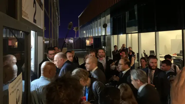 Delegates and journalists cluster outside a meeting room