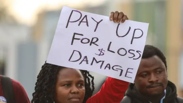 Woman holds up sign reading "Pay up for loss and damage"