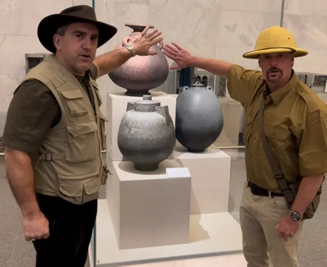 Two men stand with their hands against glass with artefacts behind