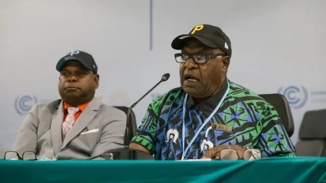 Uncle Pabai and Uncle Paul sit side by side at a press conference