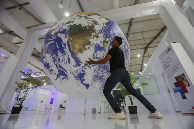 A man poses for a photo with a model of the Earth during the UN climate summit COP27 held in Sharm el-Sheikh, Egypt on 19 November 2022