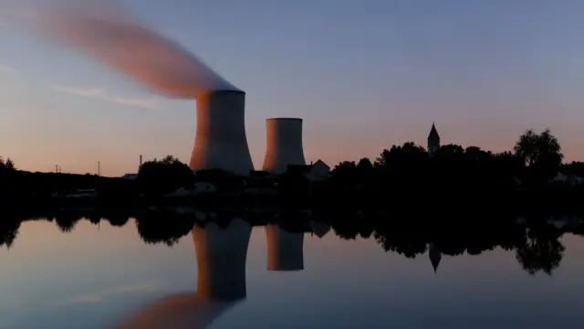 Picture of two cooling towers next to a lake, sun is setting, pink in sky