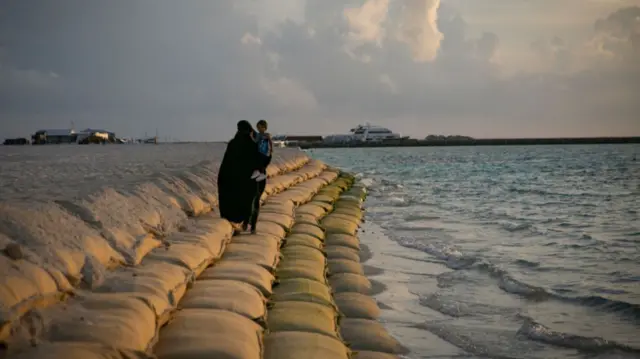 A woman walks on a wall of sandbags, placed to prevent erosion, on October 10, 2021 in Guraidhoo, Maldives.