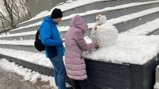 A man and a woman build a small snowman