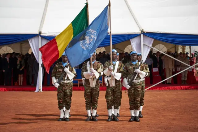 Soldiers hold the UN and Malian flags during the ceremony of Peacekeepers' Day at the operating base of MINUSMA (The United Nations Multidimensional Integrated Stabilization Mission in Mali) in Bamako on May 29, 2018