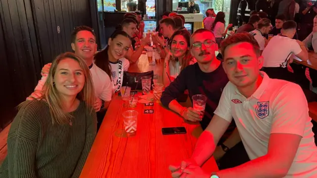 Tessa and Tom and their friends sit around a table in a pub