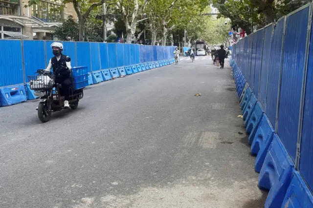 People ride past barriers set up along a road, where protests against coronavirus disease (COVID-19) curbs took place following the deadly Urumqi fire, in Shanghai, China November 28, 2022