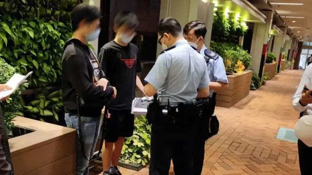 Two police officers (centre) questions two mainland Chinese students (left) who were reportedly handing out leaflets with details of the deadly 24th November Urumqi fire at the campus of the University of Hong Kong, 27 Nov 2022.