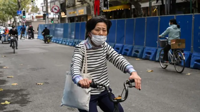 People ride bicycles past barricades on a street next to Wulumuqi street