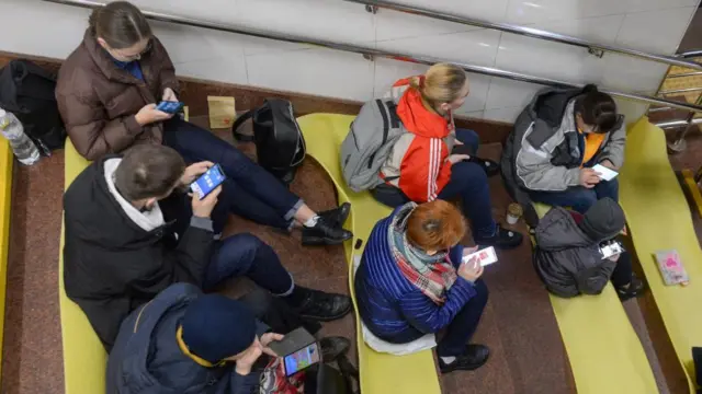 People check their phones as they shelter inside a metro station after a shelling in Kyiv