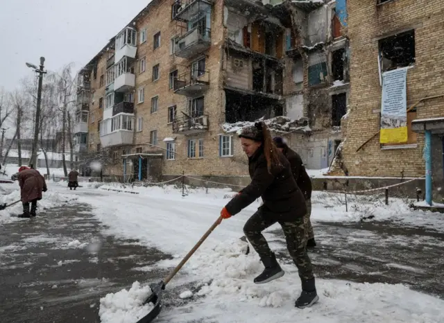 Ukrainians clear away snow from a road