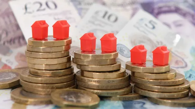 A photo of board game plastic houses perched on top of stacks of coins