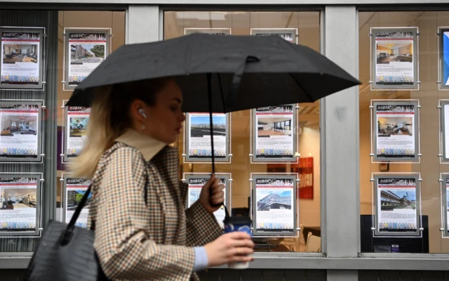 Woman walks with umbrella outside estate agent in London