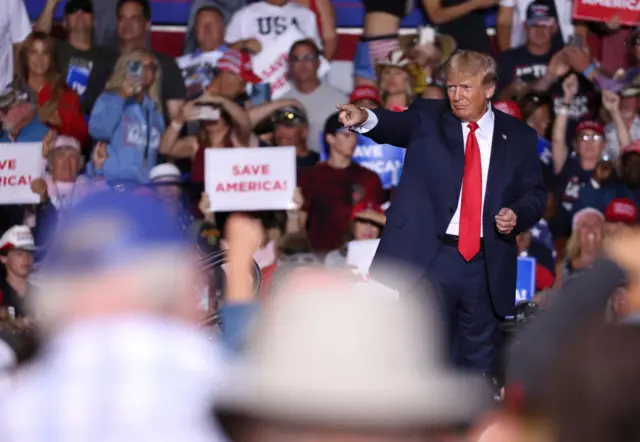 Donald Trump at a GOP rally in Nevada, with a supporter behind him holding a sign that says 'Save America'