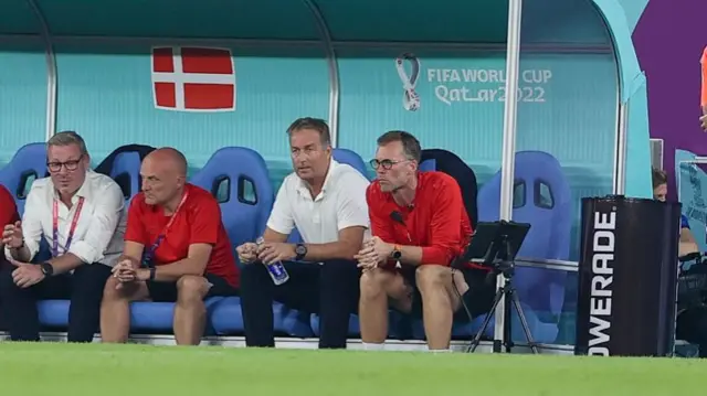 Kasper Hjulmand sits in the dugout next to a monitor