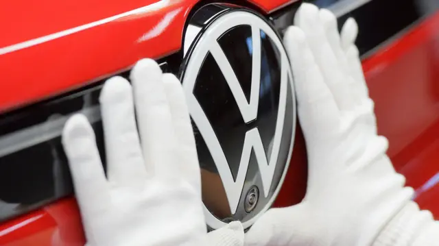 A carmaker fixes the Volkswagen logo onto a new car