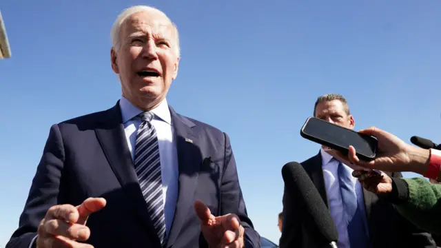 Joe Biden is surrounded by microphones as he answers questions from journalists