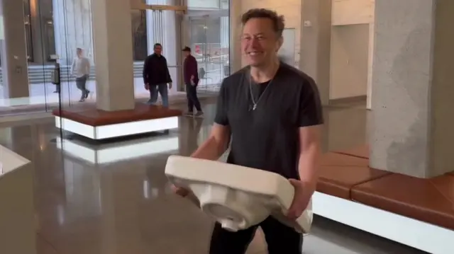 Elon Musk walking around Twitter HQ carrying a white bathroom sink