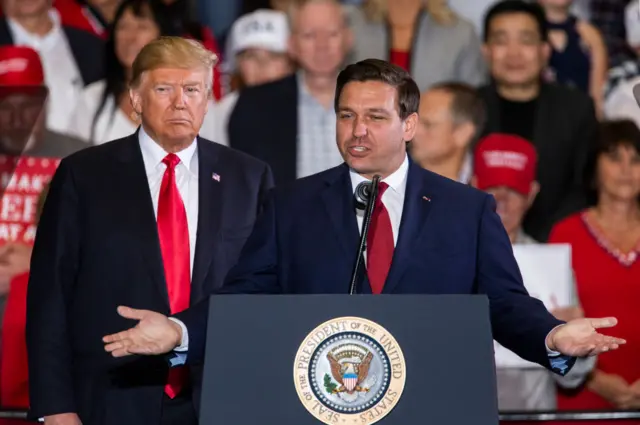 Ron DeSantis speaks with Donald Trump at a campaign rally in 2018