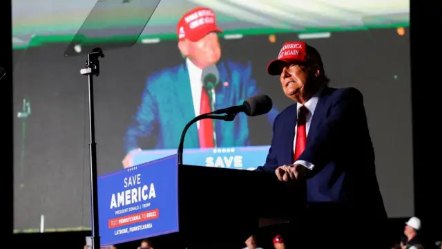 Donald Trump speaks at a podium sporting his "make America great again" hat