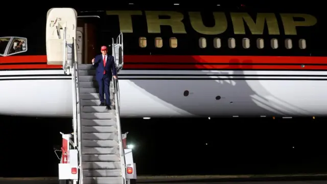 Donald Trumps walks down the steps from a plane bearing his name