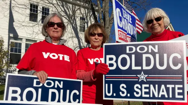 Three women holding campaign sings in support of Republican Don Bolduc in Center Conway, New Hampshire