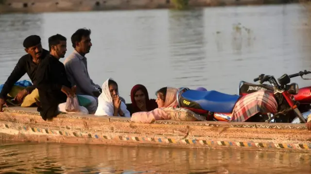 Internally displaced people use a boat to cross a flooded area at Dadu in Sindh province on 27 October, 2022